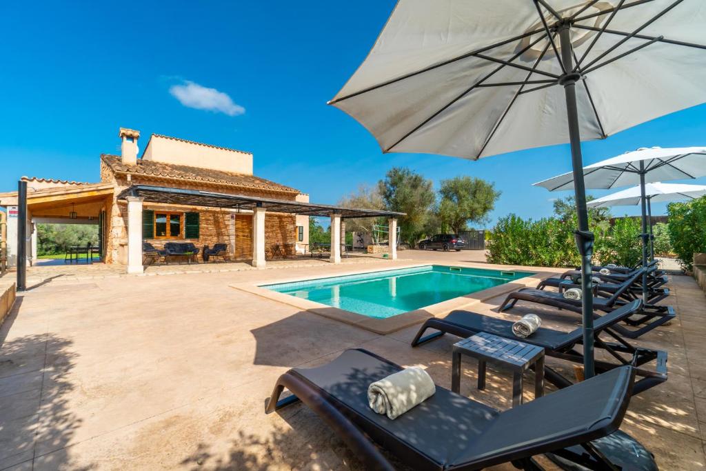 a villa with a swimming pool with chairs and an umbrella at Finca Casa BINITAREF in Sineu