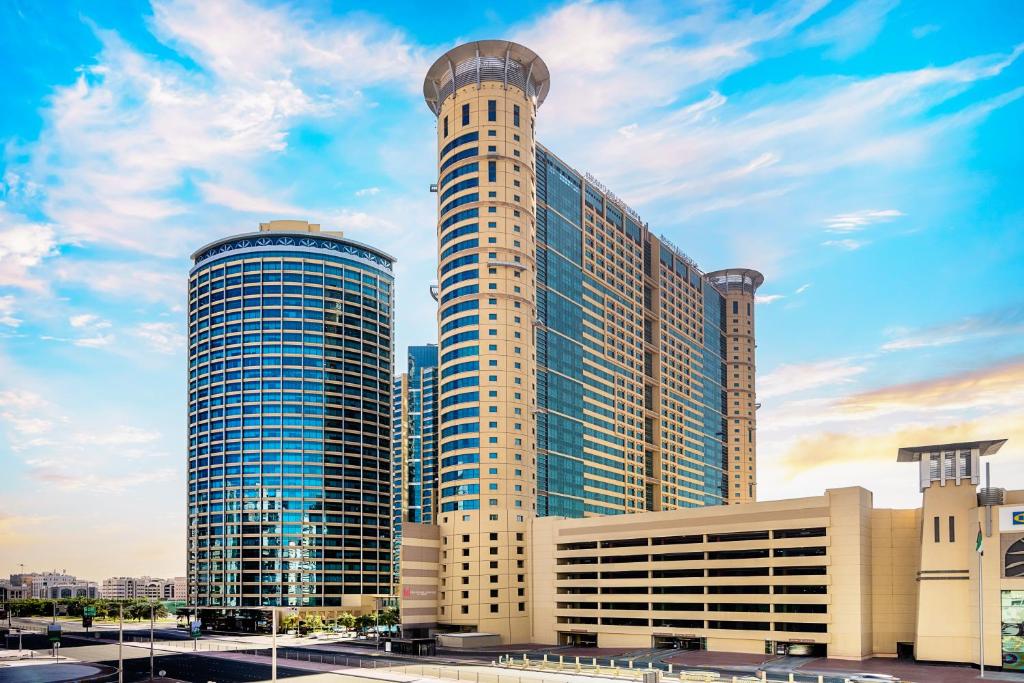 a large building with a tower in front of it at Grand Millennium Al Wahda Hotel and Executive Apartments Abu Dhabi in Abu Dhabi