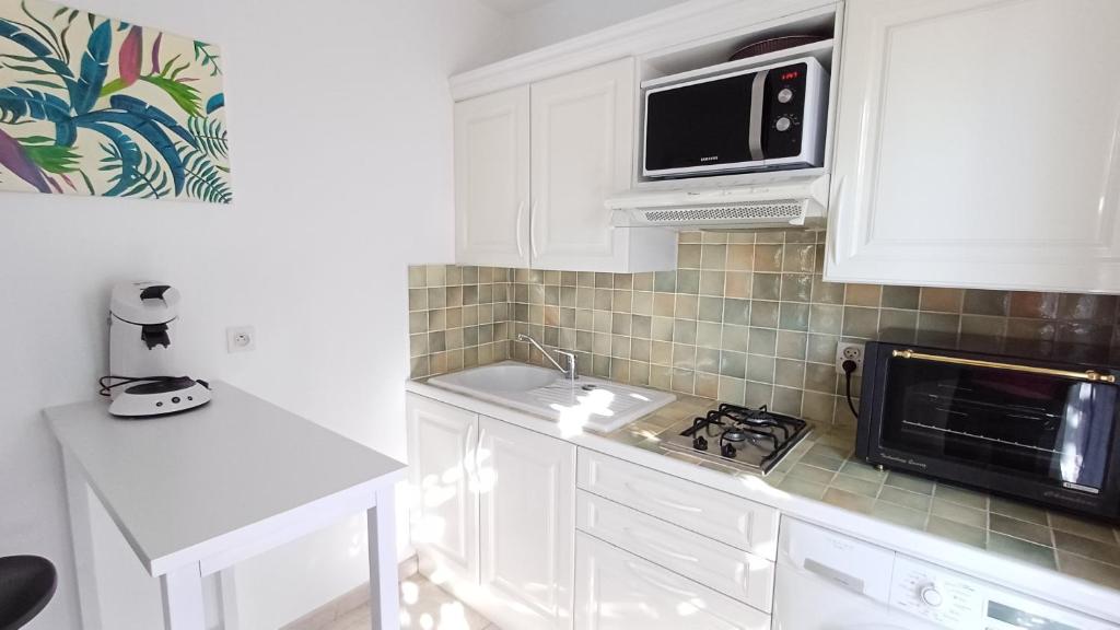 une cuisine blanche avec un évier et un micro-ondes dans l'établissement Appartement dans villa à Valescure, à Saint-Raphaël