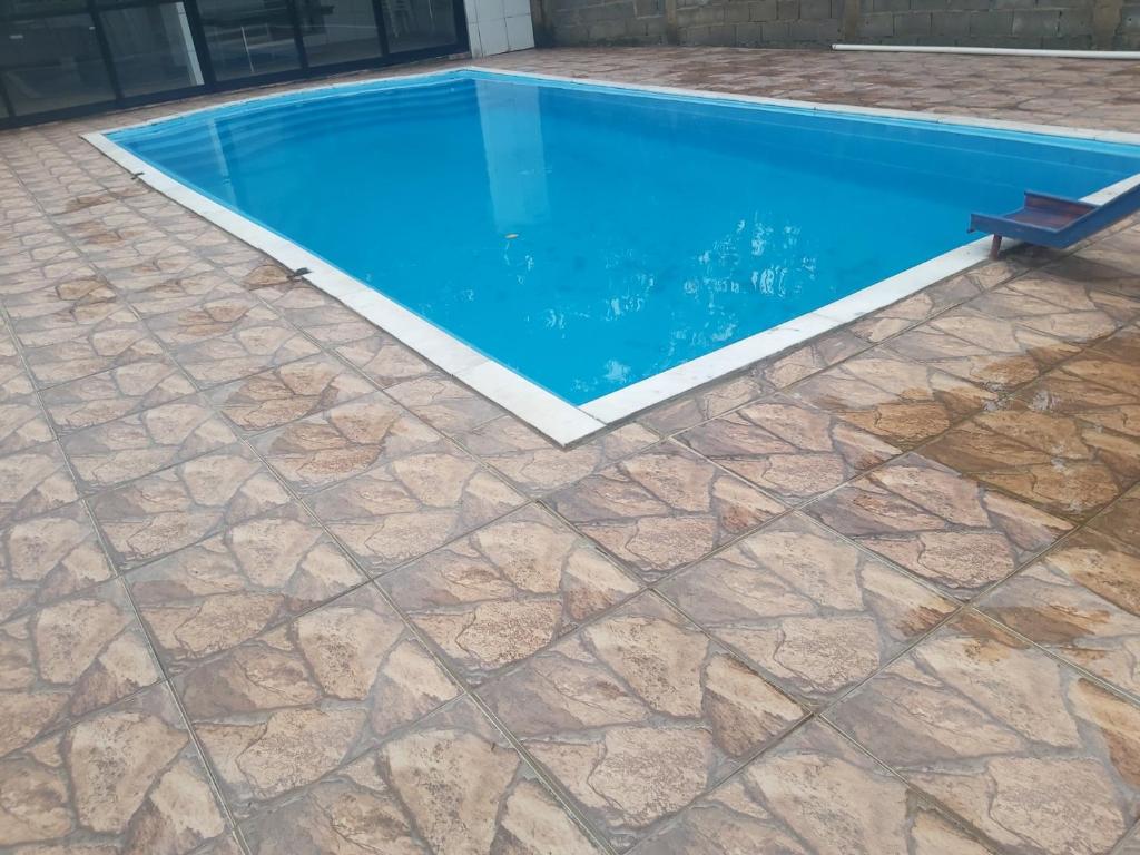 a swimming pool with a stone floor and blue water at Chacara Rancho da Cris in Ibiúna