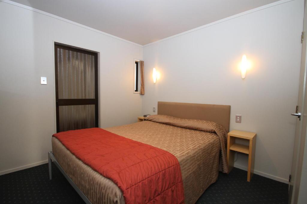 a hotel room with a bed and a red blanket at Bentleys Motor Inn in Palmerston North