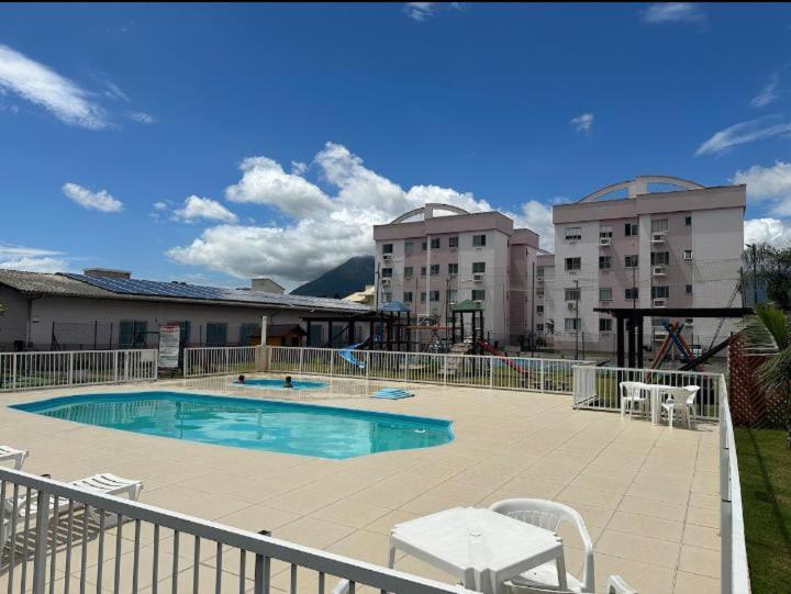 a swimming pool with white chairs and two buildings at Apto 304 sc in Palhoça