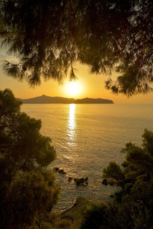a sunset over a body of water with trees at Agistri Hotel in Skala