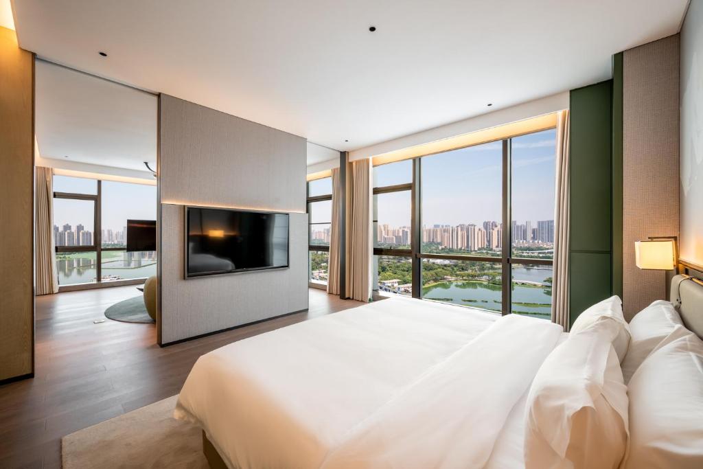a bedroom with a large bed with a tv and windows at Qinglian Jinghe Hotel Wuhan Zoo International Expo Center Branch in Han-yang-hsien