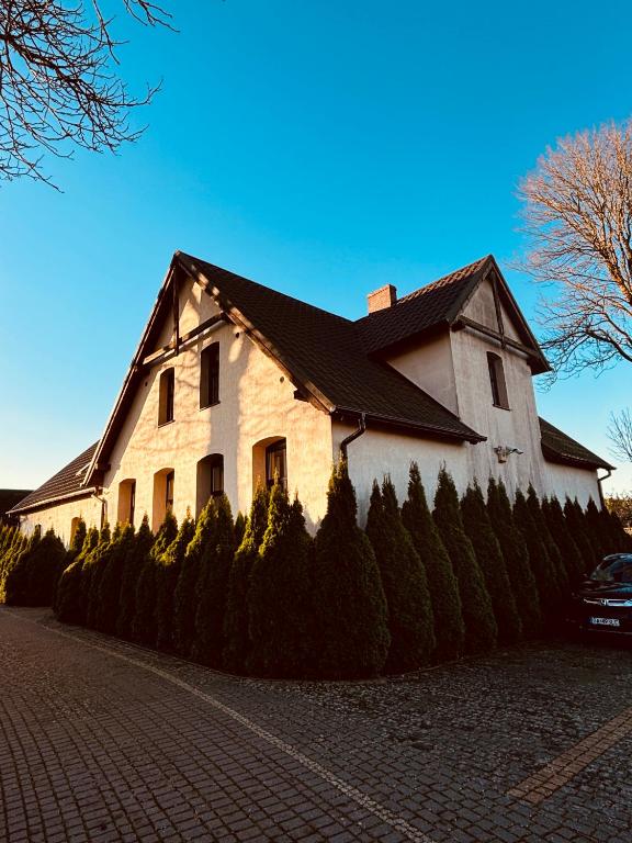 a white house with a black roof on a street at Folwark Minikowo - Agroturystyka w Borach Tucholskich - 5 pokoi z prywatnymi łazienkami in Bysław
