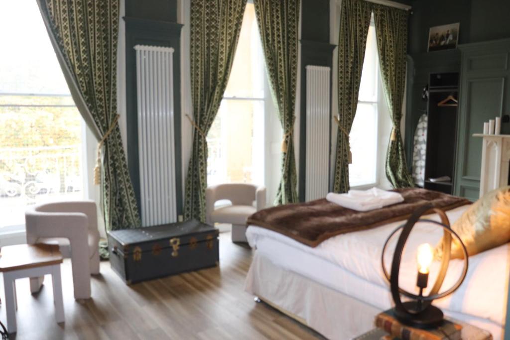a bedroom with a bed and chairs and windows at Rooms on The Prom in Cheltenham