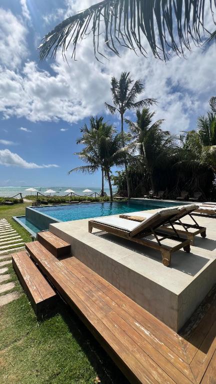 a pool with a bench and a table and palm trees at Pousada Casotas in Pôrto de Pedras