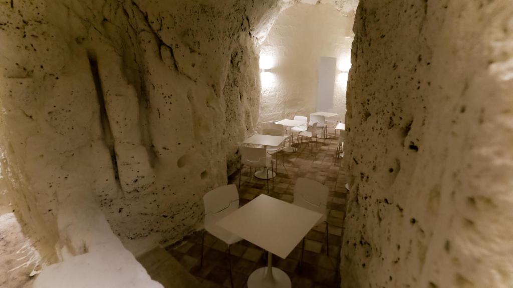 Habitación de piedra con mesa blanca y sillas en Giardini di Pietra, en Matera