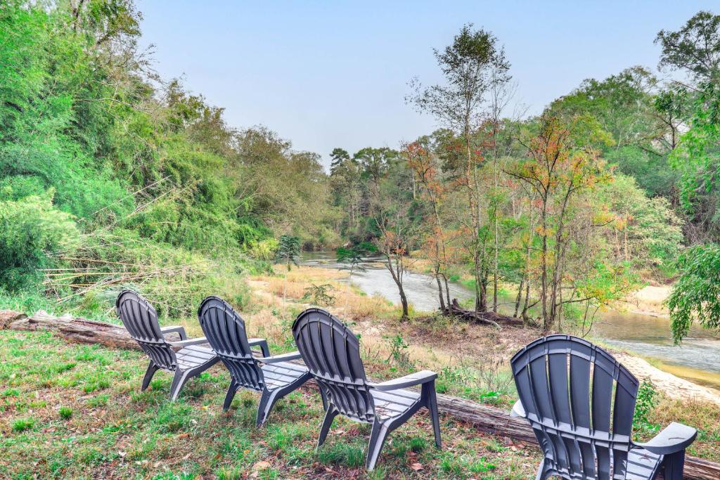 four black chairs sitting in the grass near a river at River Frontage Quiet Mississippi Vacation Rental in McComb
