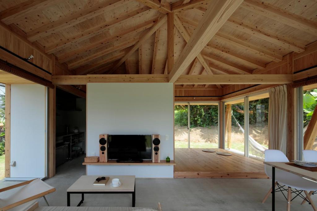 an open living room with wooden ceilings and a large screen tv at SHINMINKA Villa UTTABARU in Amami