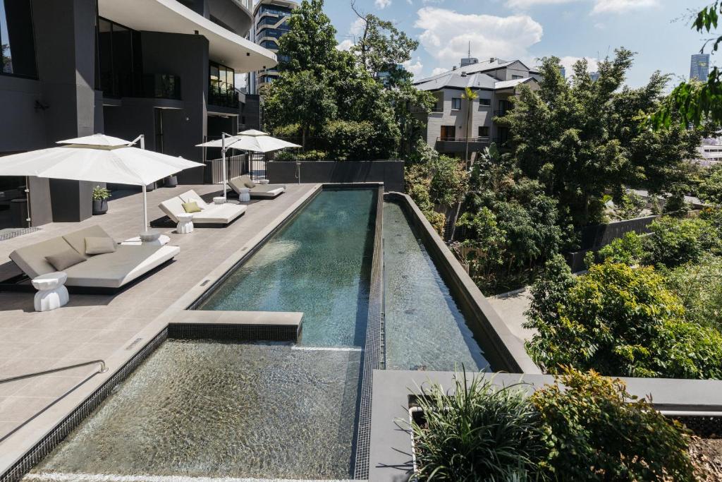 an infinity pool with chairs and umbrellas next to a building at Kangaroo Point Apartment by Urban Rest in Brisbane