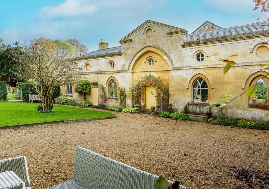 a large stone building with a yard with chairs at Artisan Hall: 4BD Stunning Grandeur in Cotswolds in Toddington