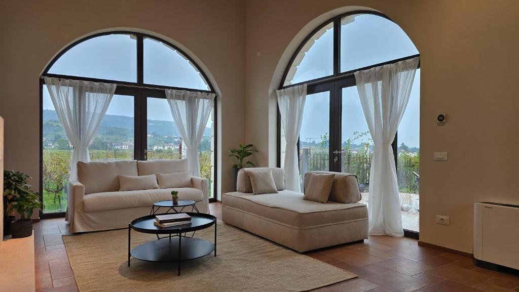 a living room with two windows and a couch and a table at Agriturismo Igino - Camera in Casale con cucina condivisa e spazi comuni, giardino, patio, parcheggio, wineshop, wifi - Immerso nei vigneti in Negrar