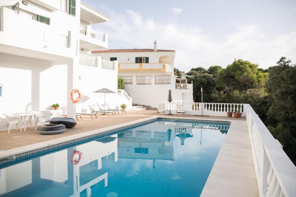 a villa with a swimming pool in front of a house at Apartamentos Gama in Cala Galdana