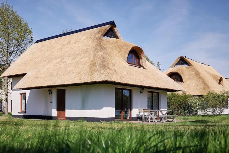 una casa con tetto di paglia, tavolo e sedie di Ferienhaus im Van der Valk Resort in Linstow a Dobbin-Linstow