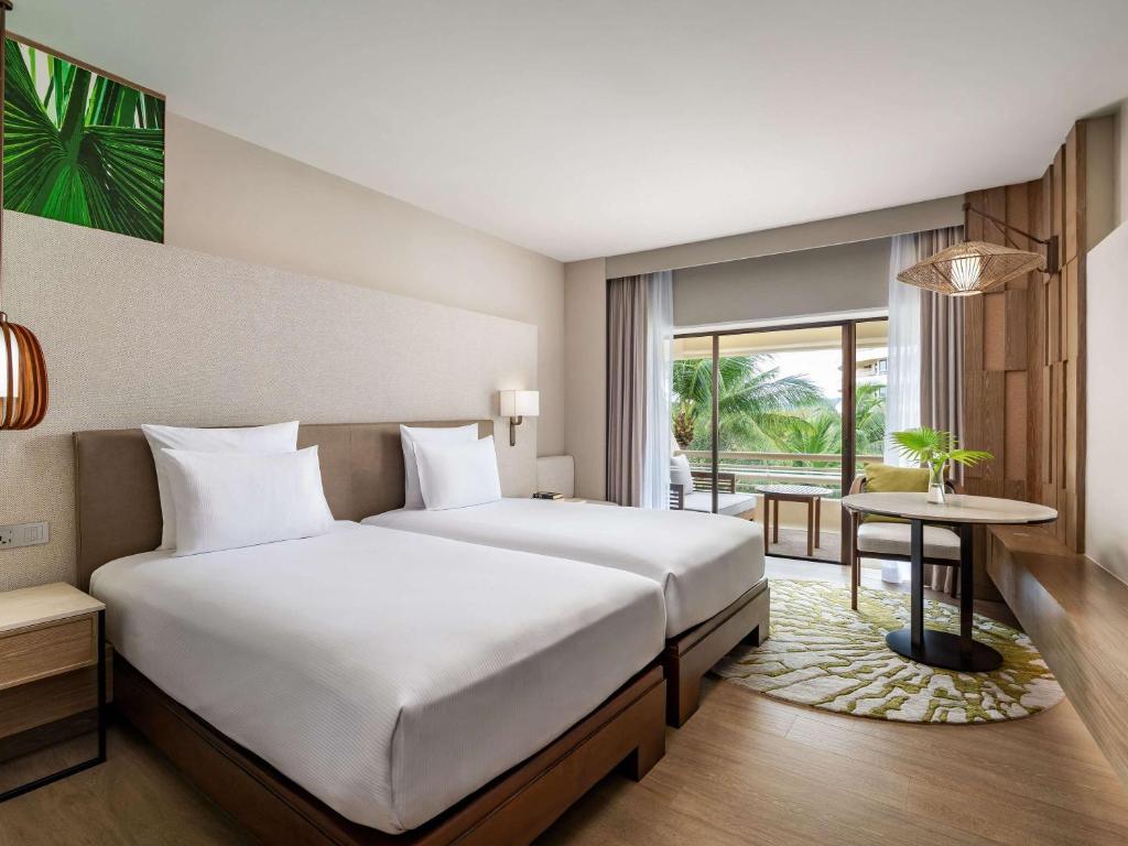 a bedroom with a large white bed and a table at Pullman Phuket Karon Beach Resort in Karon Beach