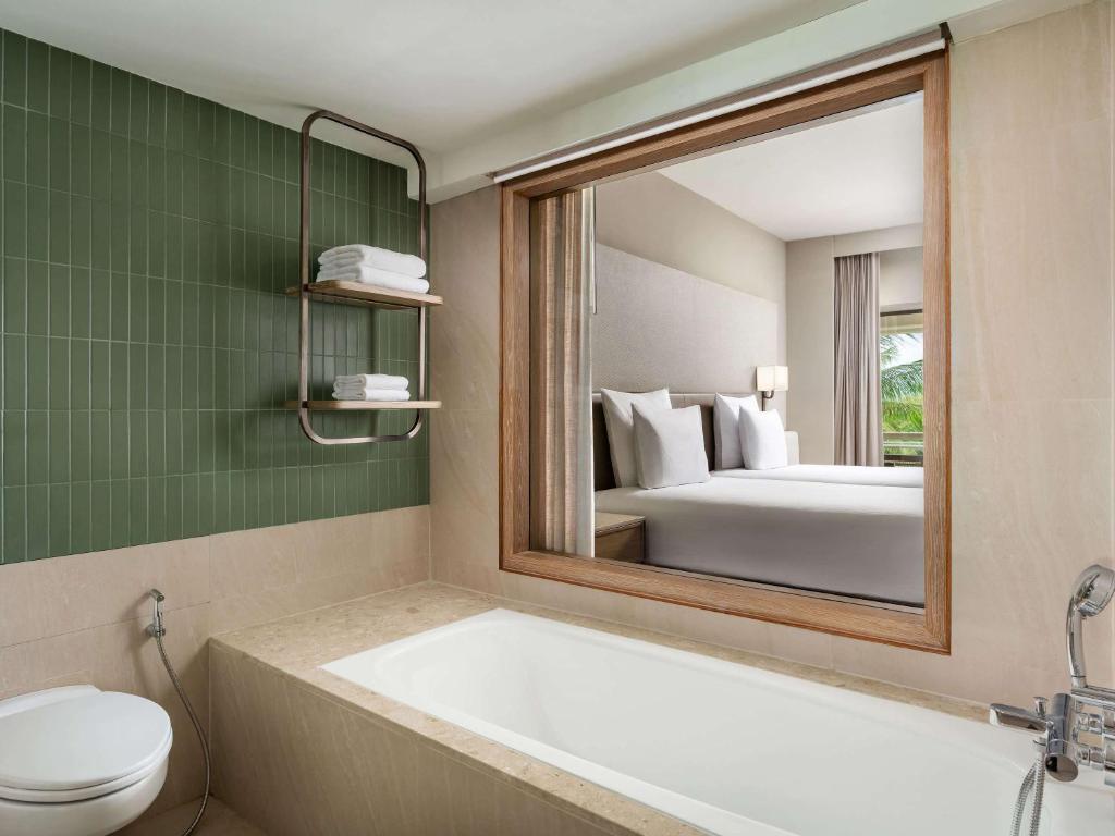 a bathroom with a tub and a toilet and a mirror at Pullman Phuket Karon Beach Resort in Karon Beach