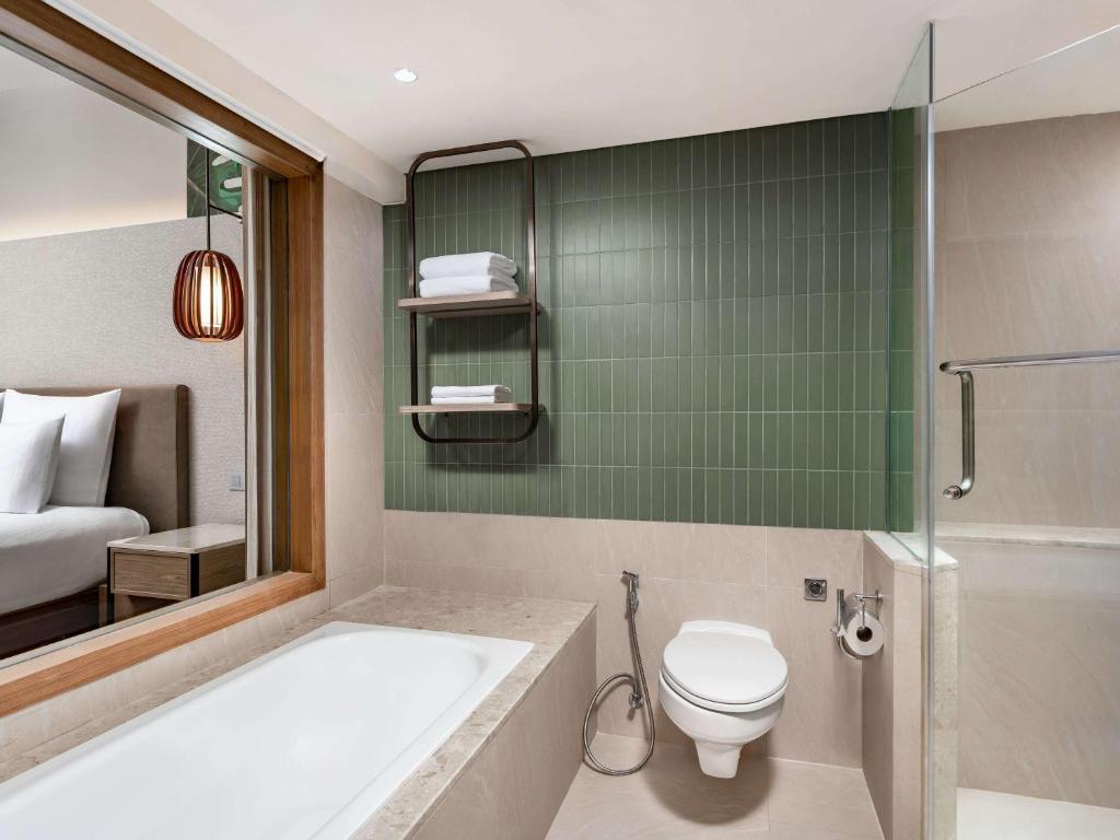 a bathroom with a tub and a toilet and a bed at Pullman Phuket Karon Beach Resort in Karon Beach