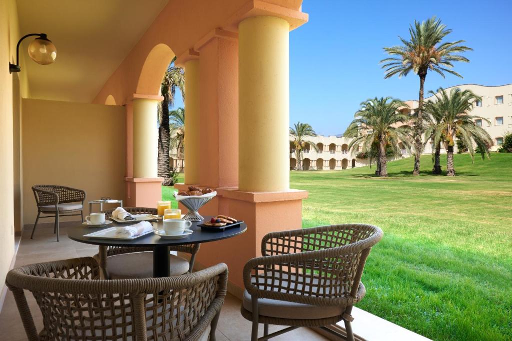 a table and chairs on a porch with palm trees at Almar Timi Ama Resort & Spa in Villasimius