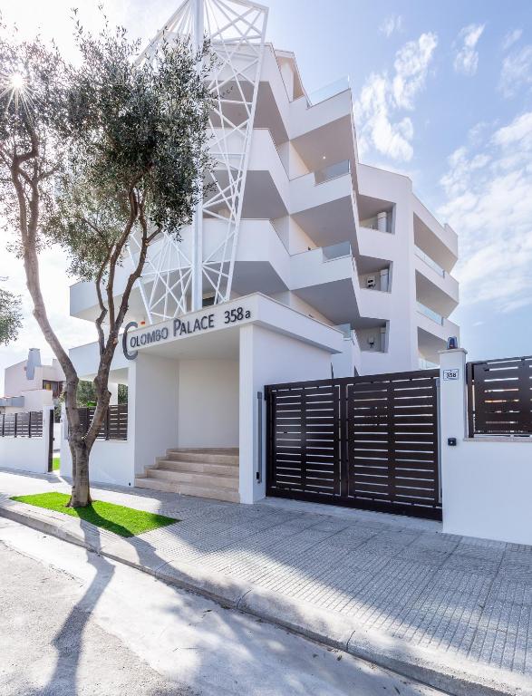 a white building with a gate and a tree at Colombo Palace - viale colombo 358 in Quartu SantʼElena