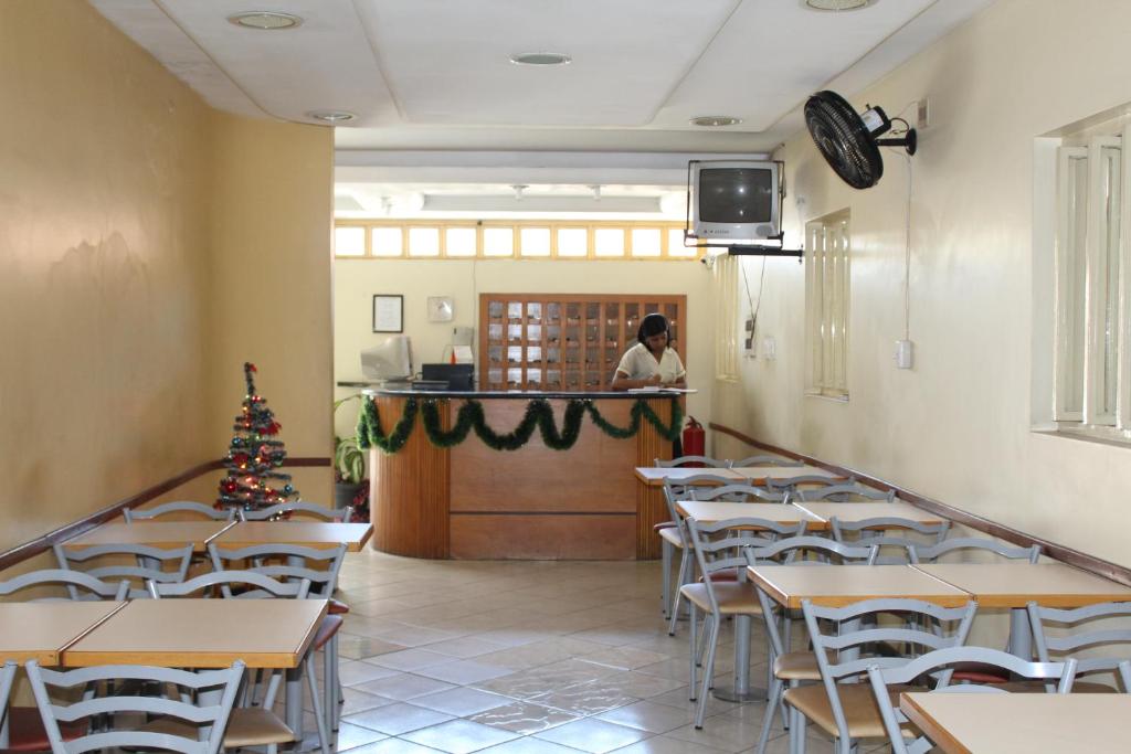 a person standing at the counter in a restaurant with tables and chairs at Hotel Aquarius in Coronel Fabriciano