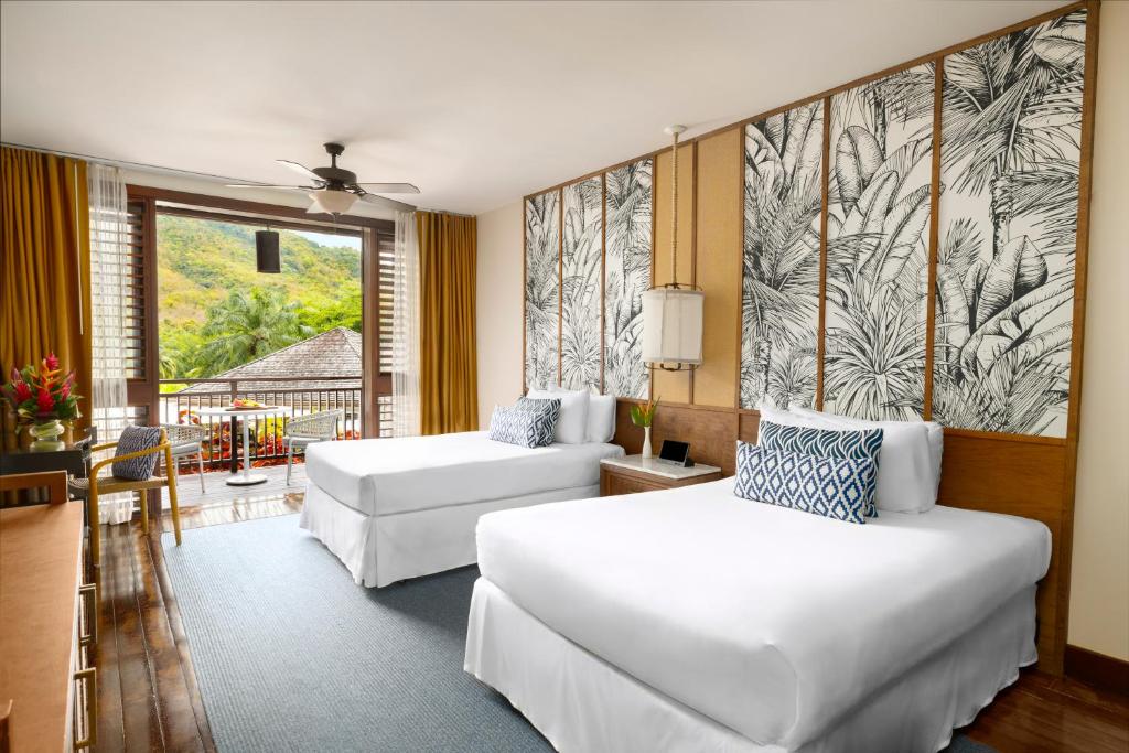 Double queen bedroom suite with balcony view, botanical wall art, and modern furnishings.