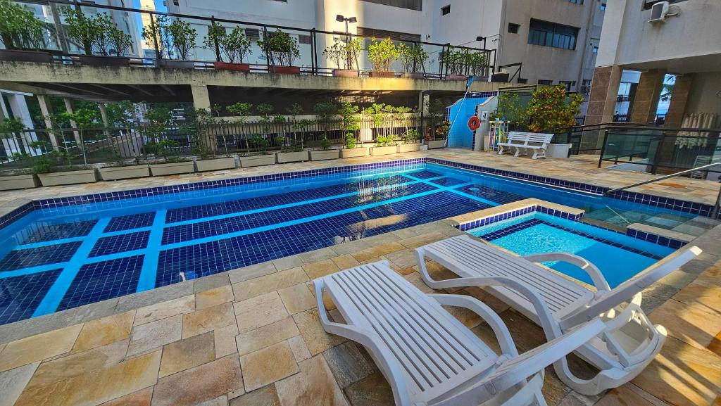 a swimming pool with two white chairs and a swimming pool at Linda Vista do Mar - Espaçoso - Praia Pitangueiras in Guarujá