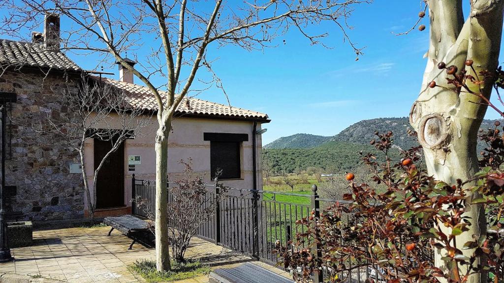 a house with a tree in front of a fence at Casa con piscina en Parque Nacional de Cabañeros in Navas de Estena