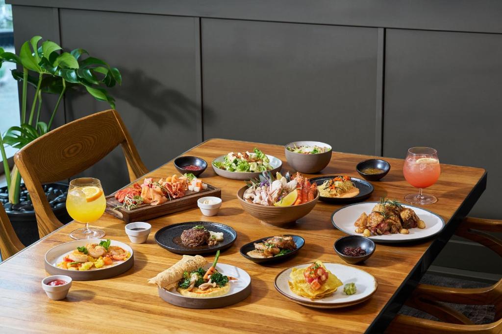 A generously laid wooden dining table filled with plated dishes, fruit, sauces and drinks.