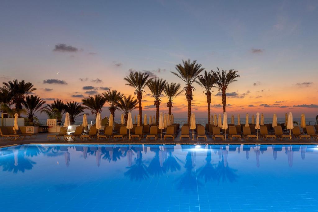 a pool with chairs and palm trees and a sunset at Queens Bay Hotel in Paphos