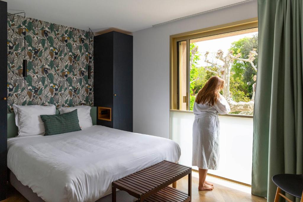 a woman looking out the window of a bedroom at Hôtel 96 in Marseille
