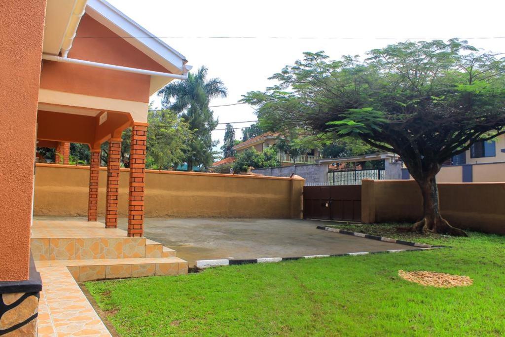 a house with a yard with a tree next to it at POPPI HOUSE 3 bedroom in Kampala