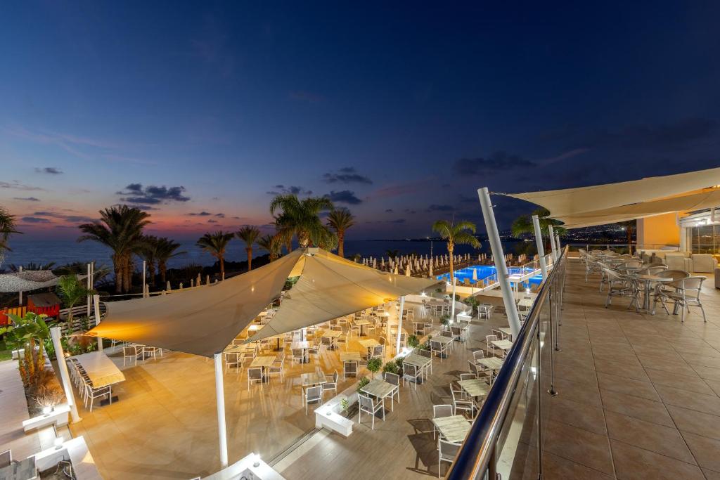 a deck with tables and chairs on a beach at night at Queens Bay Hotel in Paphos