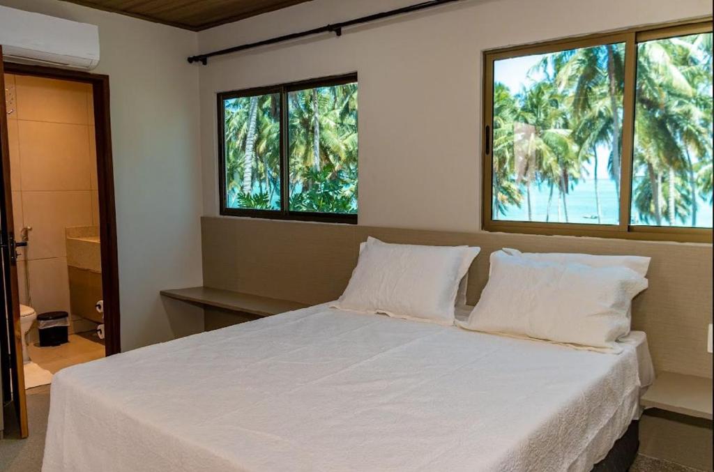 a bedroom with a white bed with two windows at Aconchego Dona Quita in São Miguel dos Milagres