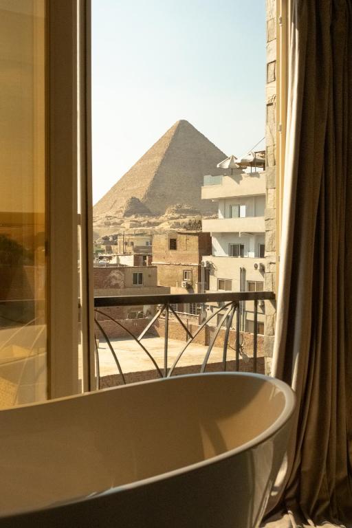 a bath tub in front of a window with a view of a pyramid at Jimmy Pyramids Hotel in Cairo