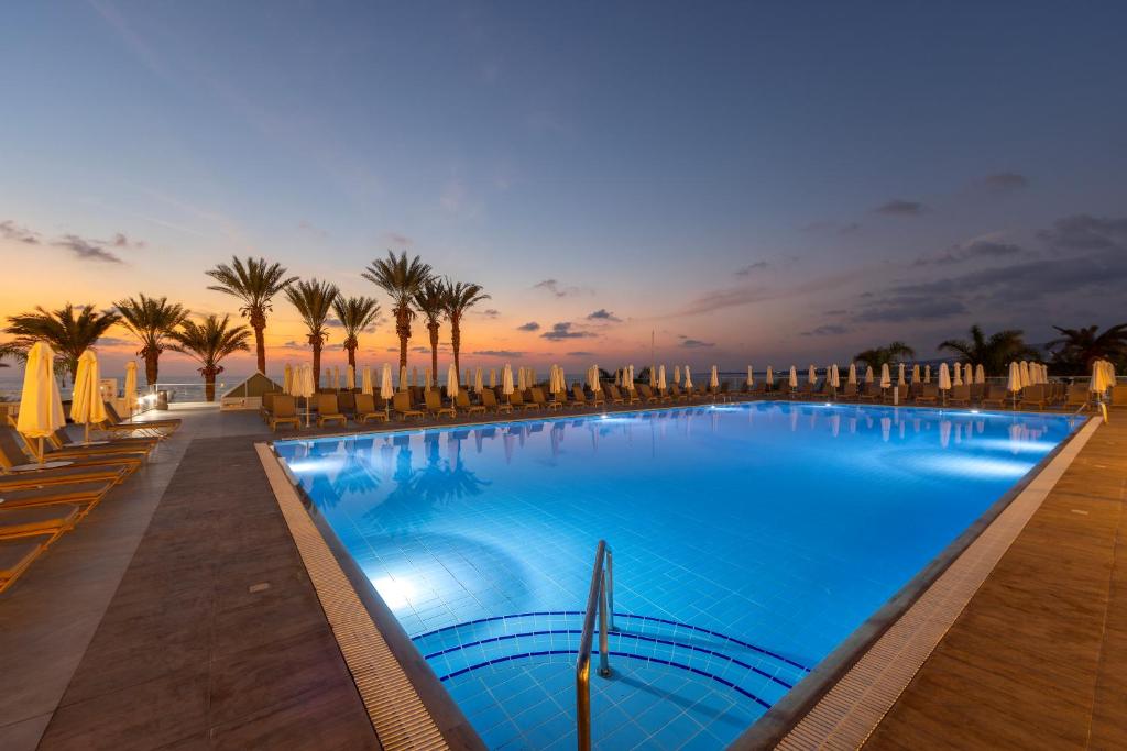 a large swimming pool with palm trees and umbrellas at Queens Bay Hotel in Paphos