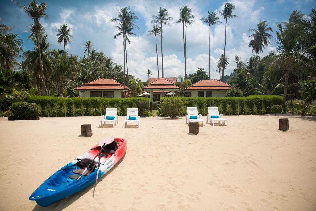 un barco y sillas en una playa con palmeras en Baan Tawan Chai, en Laem Set Beach