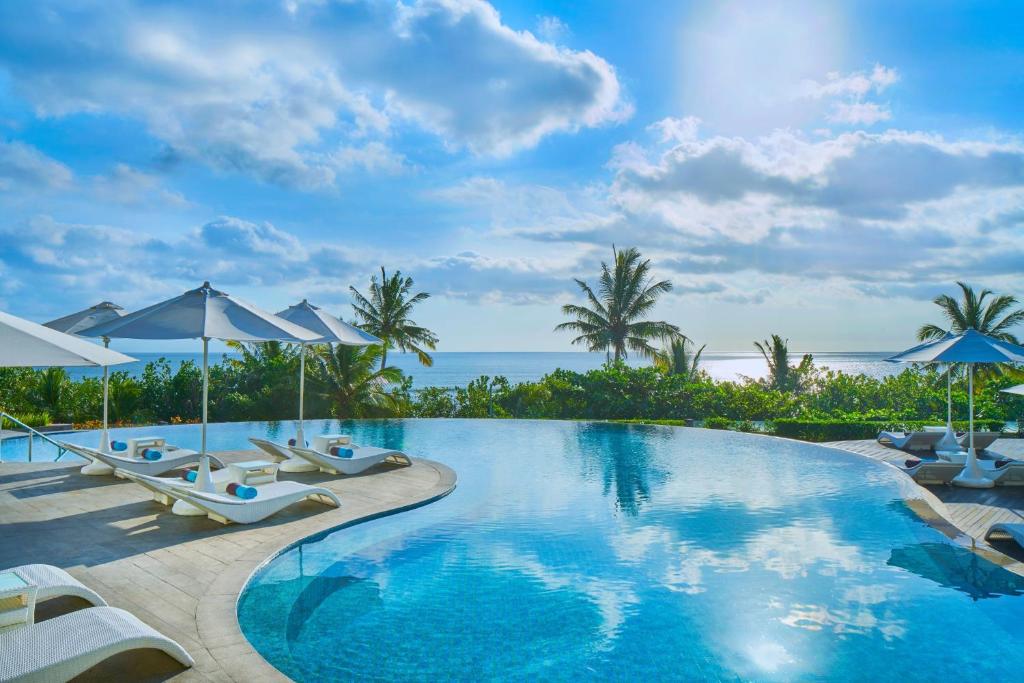 a swimming pool with chairs and umbrellas and the ocean at Sheraton Bali Kuta Resort in Kuta