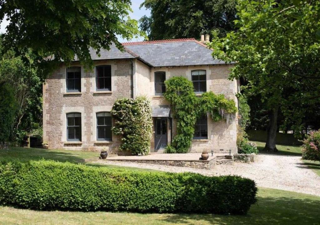 North CerneyにあるTrinity Farmhouse - Stunning House & Gardens!の茂みの古い石造りの家