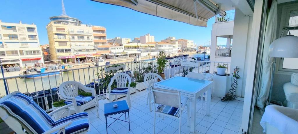 a balcony with white chairs and tables and a view of a city at Chez Ginou Vue imprenable sur le canal et la mer in Palavas-les-Flots