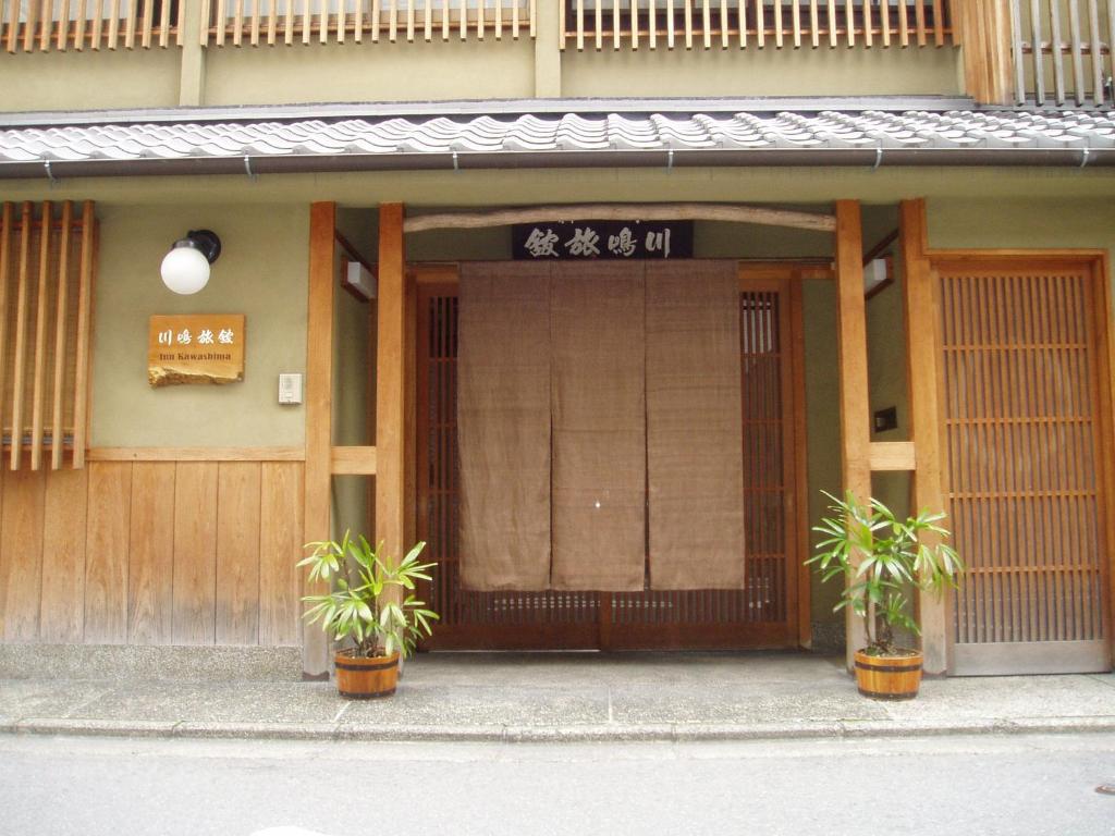 une porte d'entrée d'un bâtiment avec deux usines devant dans l'établissement Inn Kawashima, à Kyoto