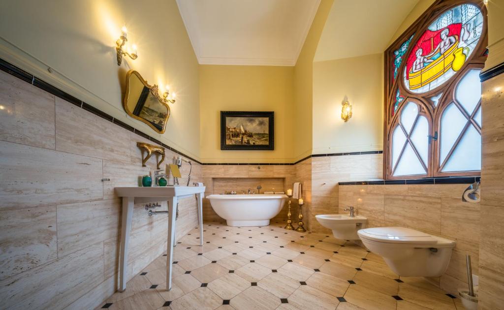 Luxurious marble bathroom with freestanding tub, stained-glass arched window, gold fixtures, and warm ambient lighting.