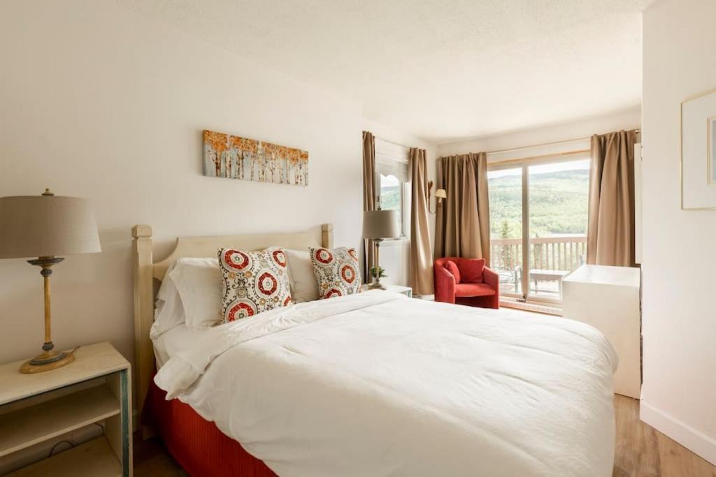 a bedroom with a white bed and a red chair at InstantSuites- The Mountain Lake house in Mont-Tremblant