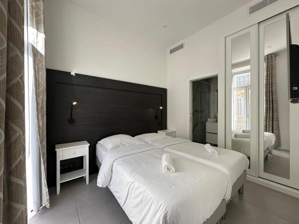 - une chambre avec 2 lits blancs et une tête de lit noire dans l'établissement B080- À l'étroit à l'hôtel Bienvenue chez nous, à Cannes