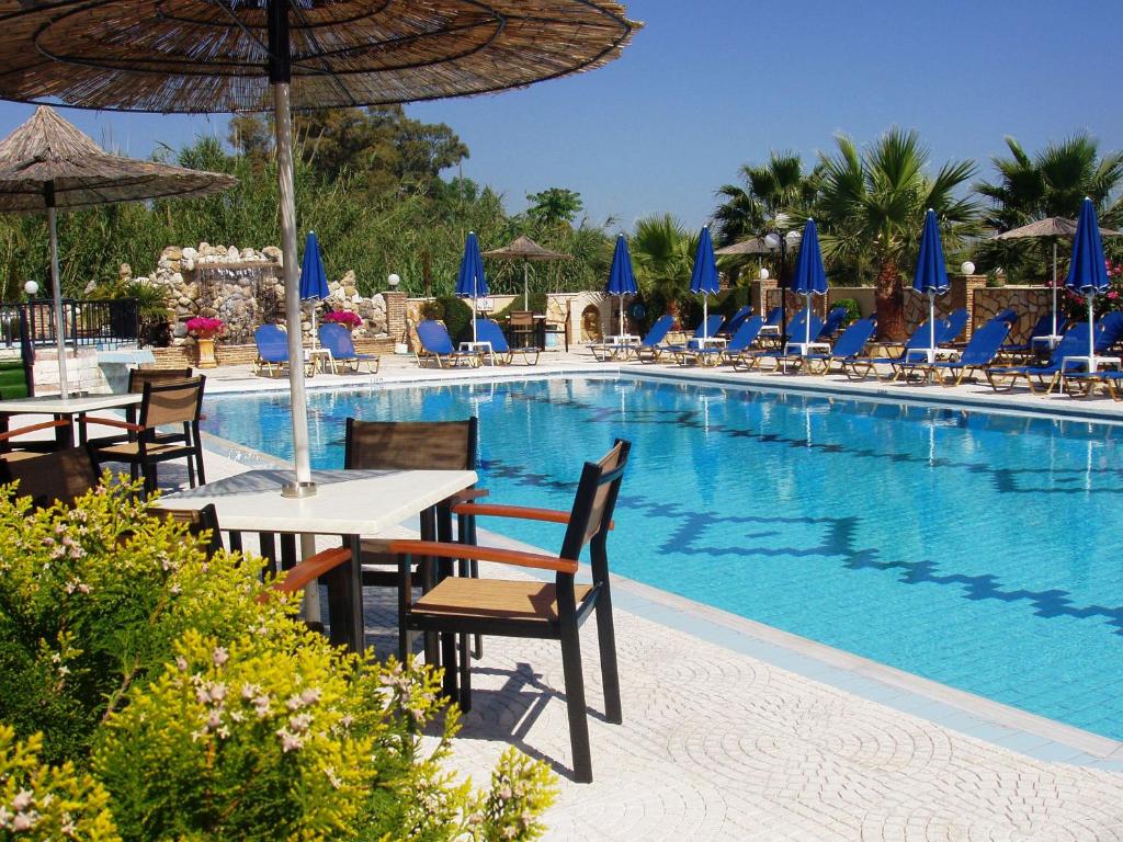 a swimming pool with tables and chairs and blue umbrellas at Paradise Apartments in Laganas