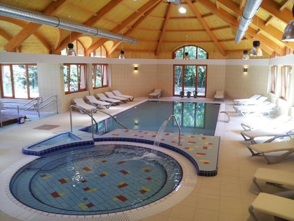 a large swimming pool in a building with chairs at Fenyves Hotel Békéscsaba in Békéscsaba