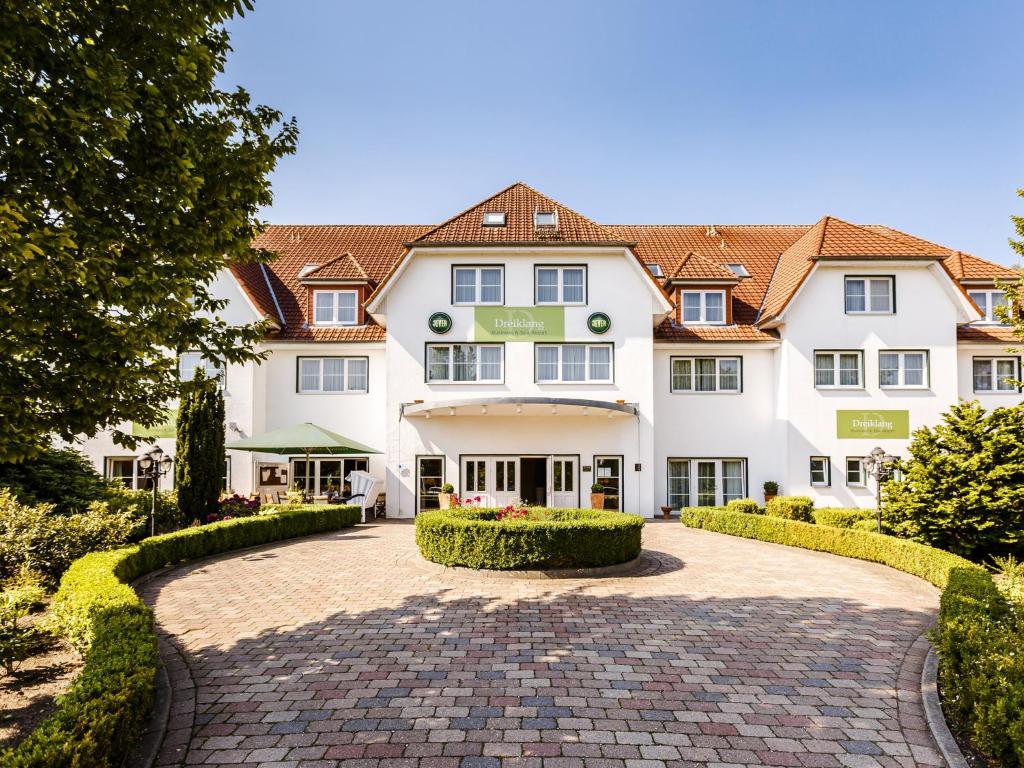 a large white building with a brick driveway at Dreiklang Business & Spa Resort in Kaltenkirchen