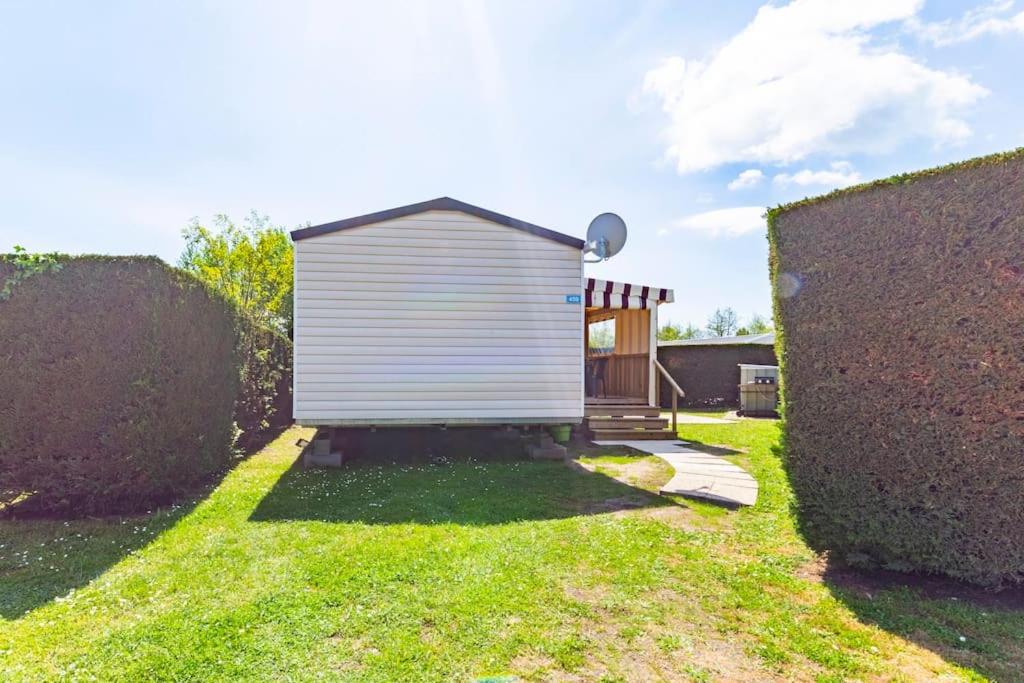 un petit hangar blanc dans une cour à côté d'une haie dans l'établissement Mobilhome confortable, spacieux et lumineux dans camping, aux Mathes
