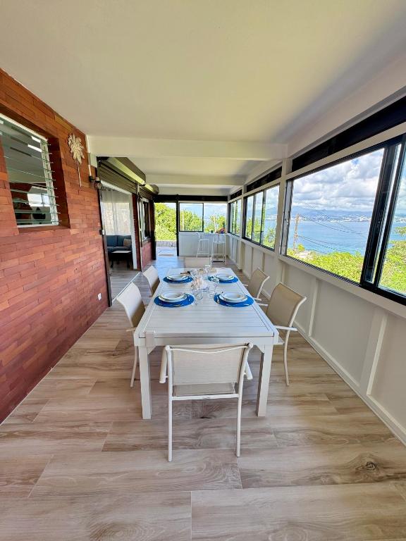 una sala da pranzo con tavolo, sedie e finestre di La villa Azur classée 3 étoiles Moderne et Confortable à deux pas de la plage de l Anse à l Ane Trois Îlets - Service Petit Dej sur demande a Les Trois-Îlets