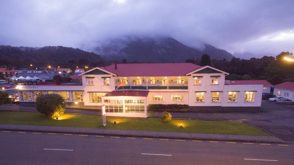 a large white building with a mountain in the background at Heartland Hotel Fox Glacier in Fox Glacier